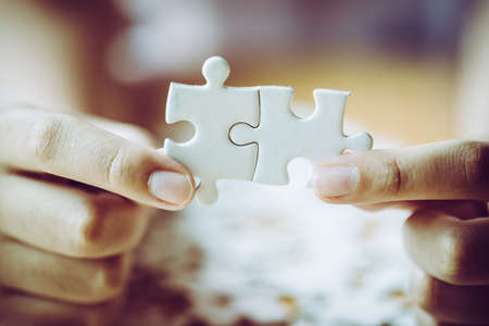 Hands of a person little child and parent playing jigsaw puzzle piece game together on wooden table...