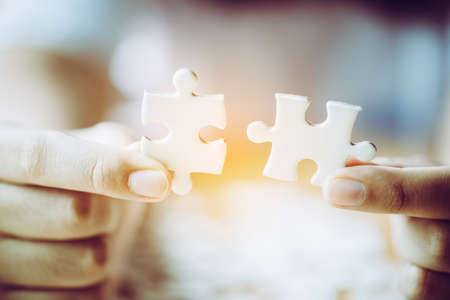 Hands of a person little child and parent playing jigsaw puzzle piece game together on wooden table at home, concept for leisure with family, play with children's development, education and fun.の写真素材