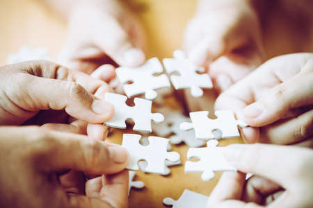 Hands of a person little child and parent playing jigsaw puzzle piece game together on wooden table at home, concept for leisure with family, play with children's development, education and fun.の写真素材