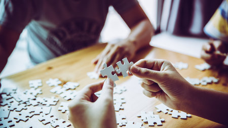 Hands of a person little child and parent playing jigsaw puzzle piece game together on wooden table at home, concept for leisure with family, play with children's development, education and fun.の写真素材