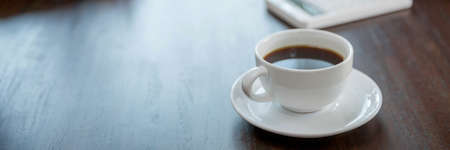 Close up white coffee cup on business black wood table near window in office.の写真素材