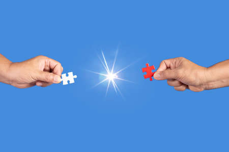Hands holding jigsaw puzzles piece with clear blue background, success business, solution strategy, teamwork partnership conceptの写真素材
