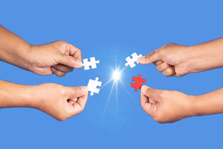 Hands holding jigsaw puzzles piece with clear blue background, success business, solution strategy, teamwork partnership conceptの写真素材