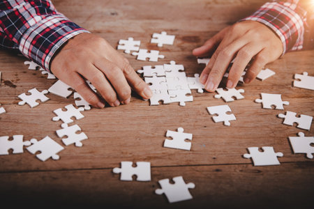 Hands holding jigsaw puzzles piece on wooden table background, success business, solution strategy, teamwork partnership conceptの写真素材