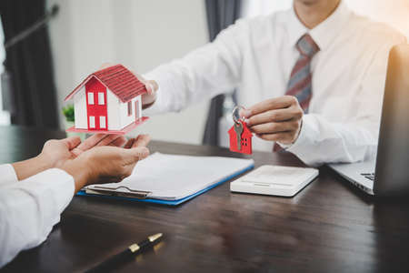 Business person hands holding home model, small building red house. Real estate agents offer contracts to purchase or rent residential. Mortgage property insurance moving home and real estate conceptの写真素材