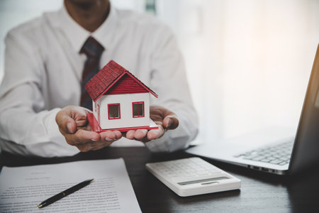Business person hands holding home model, small building red house. Real estate agents offer contracts to purchase or rent residential. Mortgage property insurance moving home and real estate conceptの写真素材
