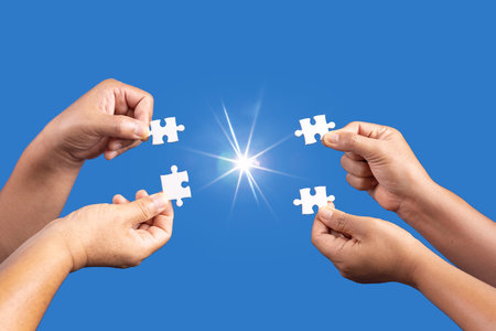 Hands holding jigsaw puzzles piece with clear blue background, success business, solution strategy, teamwork partnership conceptの写真素材