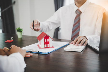 Real estate agents offer contracts to purchase or rent residential. Business person hands holding home model, small building red house. Mortgage property insurance moving home and real estate conceptの写真素材