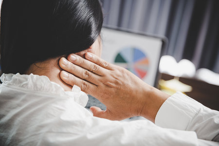 Young asian woman is sitting at work and has tension pain in her neck. Concept office syndrome backache pain from occupational disease, Female having muscle pain from using laptop computer, back pain.の写真素材