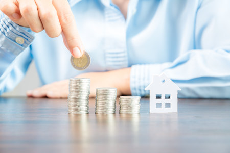 Hand holding money coins to save for residential home. cash financial plan for loans or mortgages and investments with bank. Concept for house insurance business with income tax and real estate growthの写真素材