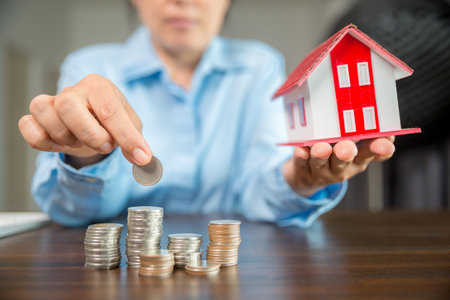 Hand holding money coins to save for residential home. cash financial plan for loans or mortgages and investments with bank. Concept for house insurance business with income tax and real estate growthの写真素材