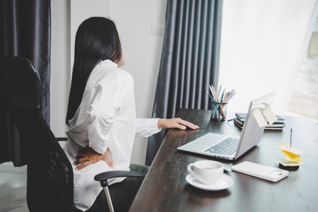 Young asian woman is sitting at work and has tension pain in her neck. Concept office syndrome backache pain from occupational disease, Female having muscle pain from using laptop computer, back pain.の写真素材