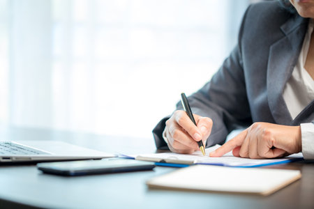 Workplace closeup person professional businesswoman sitting at desk hold pen signing or signature contract paper. Employee woman writing agreement document on paperwork form corporate at work officeの写真素材