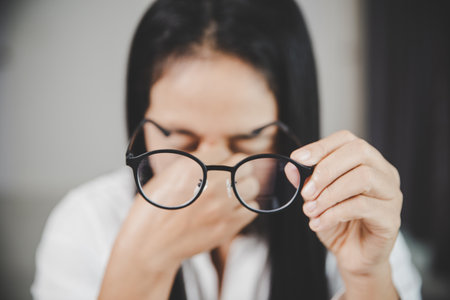 Young business woman person sleepy and has frustration eye problems with cephalalgia disease from using laptop computer on her office desk. Stressed female employee tired and exhausted from overwork.の写真素材