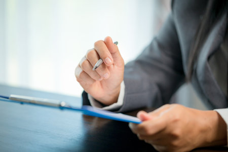 Workplace closeup person professional businesswoman sitting at desk hold pen signing or signature contract paper. Employee woman writing agreement document on paperwork form corporate at work officeの写真素材