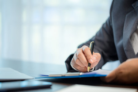 Workplace closeup person professional businesswoman sitting at desk hold pen signing or signature contract paper. Employee woman writing agreement document on paperwork form corporate at work officeの写真素材