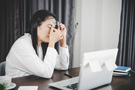 Young business woman person sleepy and has frustration eye problems with cephalalgia disease from using laptop computer on her office desk. Stressed female employee tired and exhausted from overwork.の写真素材