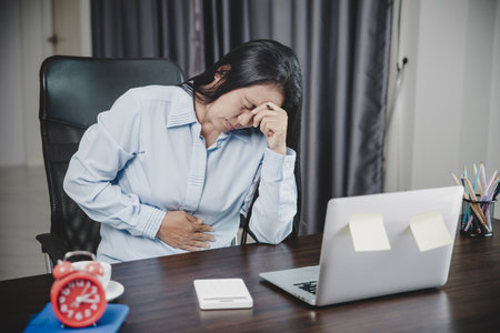 Young asian business woman person sitting at work and has stress pain in her stomach. Concept office syndrome abdomen pain from occupational disease, Female having belly pain and using laptop computerの写真素材