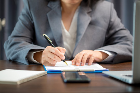 Workplace closeup person professional businesswoman sitting at desk hold pen signing or signature contract paper. Employee woman writing agreement document on paperwork form corporate at work officeの写真素材