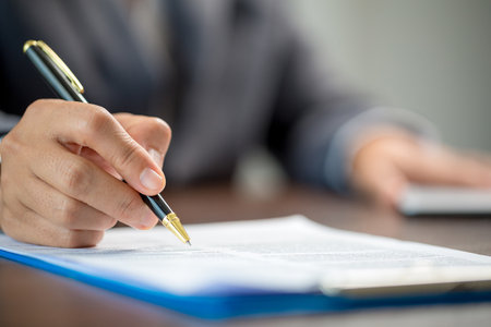 Workplace closeup person professional businesswoman sitting at desk hold pen signing or signature contract paper. Employee woman writing agreement document on paperwork form corporate at work officeの写真素材