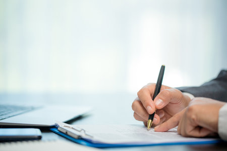 Workplace closeup person professional businesswoman sitting at desk hold pen signing or signature contract paper. Employee woman writing agreement document on paperwork form corporate at work officeの写真素材