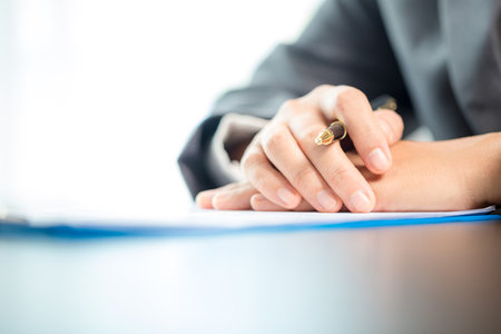 Workplace closeup person professional businesswoman sitting at desk hold pen signing or signature contract paper. Employee woman writing agreement document on paperwork form corporate at work officeの写真素材