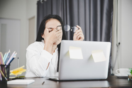 Young business woman person sleepy and has frustration eye problems with cephalalgia disease from using laptop computer on her office desk. Stressed female employee tired and exhausted from overwork.の写真素材