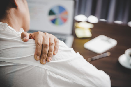 Young asian woman is sitting at work and has tension pain in her neck. Concept office syndrome backache pain from occupational disease, Female having muscle pain from using laptop computer, back pain.の写真素材