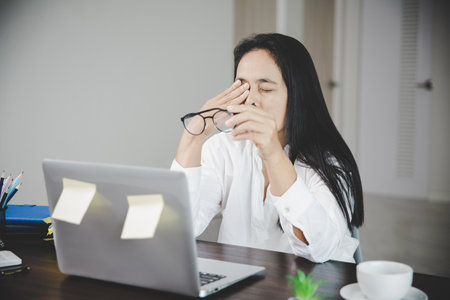 Young business woman person sleepy and has frustration eye problems with cephalalgia disease from using laptop computer on her office desk. Stressed female employee tired and exhausted from overwork.の写真素材