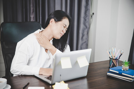 Young asian woman is sitting at work and has tension pain in her neck. Concept office syndrome backache pain from occupational disease, Female having muscle pain from using laptop computer, back pain.の写真素材