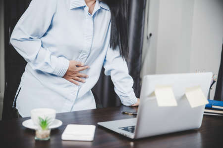 Young asian business woman person sitting at work and has stress pain in her stomach. Concept office syndrome abdomen pain from occupational disease, Female having belly pain and using laptop computerの写真素材