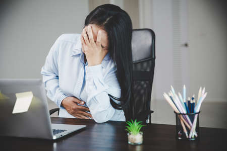 Young asian business woman person sitting at work and has stress pain in her stomach. Concept office syndrome abdomen pain from occupational disease, Female having belly pain and using laptop computerの写真素材