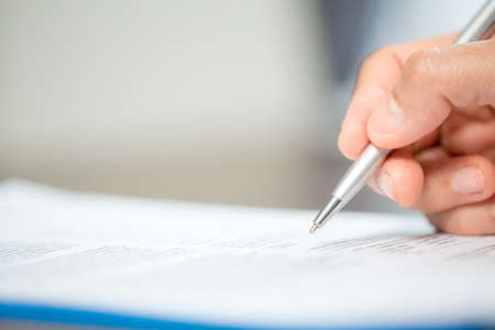 Workplace closeup person professional businesswoman sitting at desk hold pen signing or signature contract paper. Employee woman writing agreement document on paperwork form corporate at work officeの写真素材