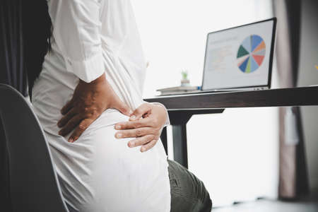 Young asian woman is sitting at work and has tension pain in her neck. Concept office syndrome backache pain from occupational disease, Female having muscle pain from using laptop computer, back pain.の写真素材