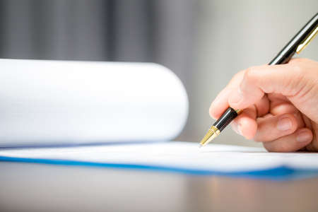 Workplace closeup person professional businesswoman sitting at desk hold pen signing or signature contract paper. Employee woman writing agreement document on paperwork form corporate at work officeの写真素材