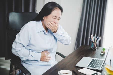 Young asian business woman person sitting at work and has stress pain in her stomach. Concept office syndrome abdomen pain from occupational disease, Female having belly pain and using laptop computerの写真素材