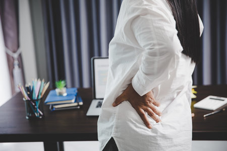 Young asian woman is sitting at work and has tension pain in her neck. Concept office syndrome backache pain from occupational disease, Female having muscle pain from using laptop computer, back pain.の写真素材