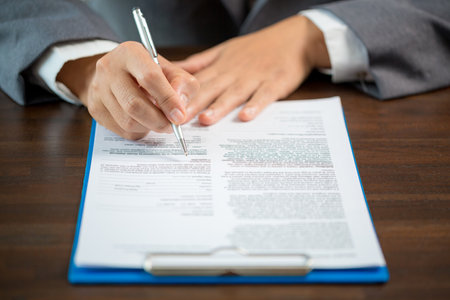 Workplace closeup person professional businesswoman sitting at desk hold pen signing or signature contract paper. Employee woman writing agreement document on paperwork form corporate at work officeの写真素材