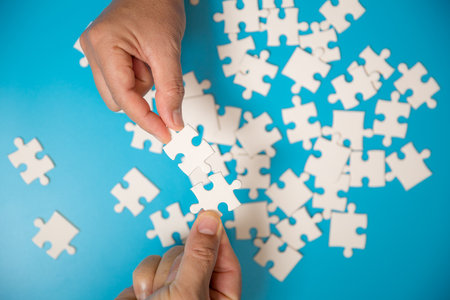 Close up hand holding and playing jigsaw game incomplete. White part of jigsaw puzzle pieces on blue background. concepts of problem solving, business, teamwork.の写真素材