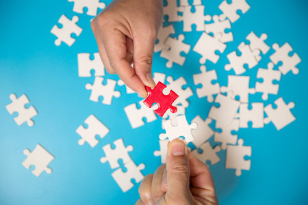 Close up hand holding and playing jigsaw game incomplete. White part of jigsaw puzzle pieces on blue background. concepts of problem solving, business, teamwork.の写真素材