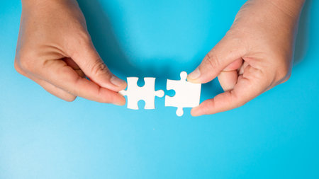 Close up hand holding and playing jigsaw game incomplete. White part of jigsaw puzzle pieces on blue background. concepts of problem solving, business, teamwork.の写真素材
