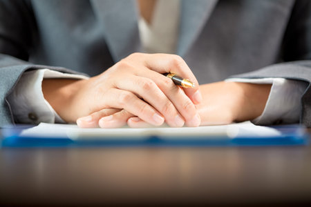 Workplace closeup person professional businesswoman sitting at desk hold pen signing or signature contract paper. Employee woman writing agreement document on paperwork form corporate at work officeの写真素材
