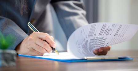 Workplace closeup person professional businesswoman sitting at desk hold pen signing or signature contract paper. Employee woman writing agreement document on paperwork form corporate at work officeの写真素材