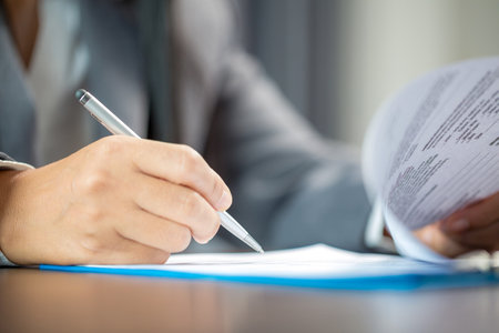 Workplace closeup person professional businesswoman sitting at desk hold pen signing or signature contract paper. Employee woman writing agreement document on paperwork form corporate at work officeの写真素材