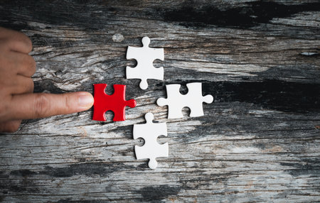 Pieces of jigsaw puzzle in woman's hands. White details of jigsaw puzzle piece on wooden background. Concept of working together as a business team. The idea of getting involved, working for success.の写真素材