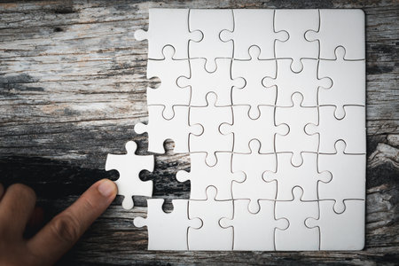 Pieces of jigsaw puzzle in woman's hands. White details of jigsaw puzzle piece on wooden background. Concept of working together as a business team. The idea of getting involved, working for success.の写真素材