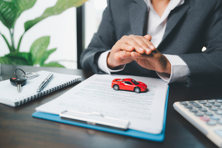 Business woman's hand protecting red toy car on desk. Planning to manage transportation finance costs. Concept of car insurance business, saving buy - sale with tax and loan for new car.の写真素材