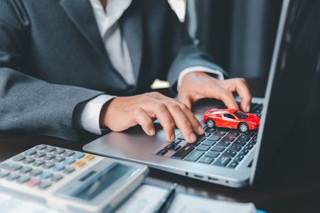 Close-up of a small red car on laptop keypad. Planning to manage transportation finance costs. Concept of car insurance business, saving buy with tax and loan for new car.の写真素材
