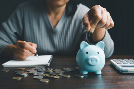 Business asian woman hand put coins in piggy bank on wood table background, saving money wealth and financial concept, finance, investment, Financial planning.Financial planning deposit for retirementの写真素材