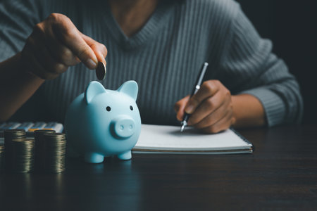Business asian woman hand put coins in piggy bank on wood table background, saving money wealth and financial concept, finance, investment, Financial planning.Financial planning deposit for retirementの写真素材